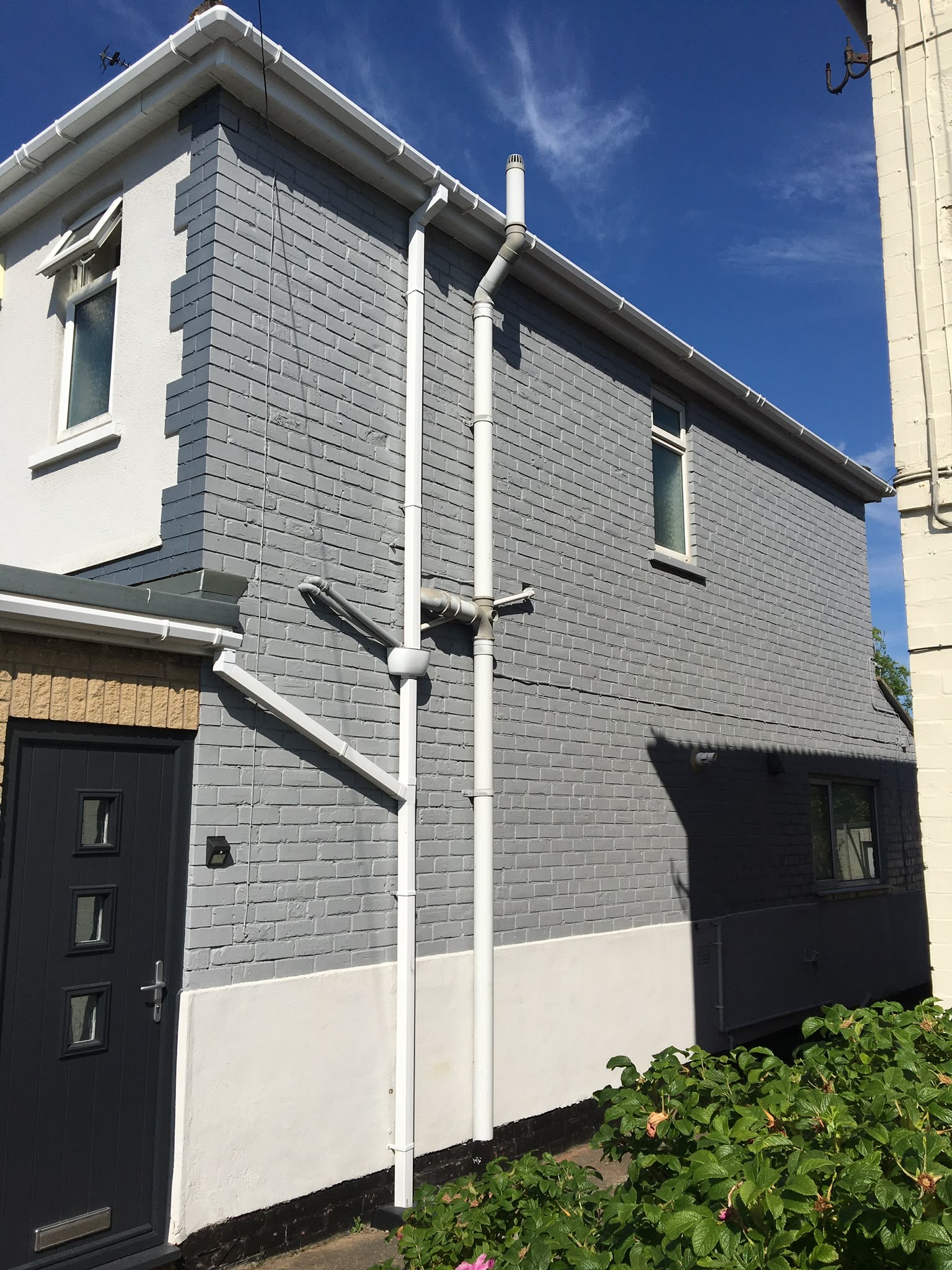 Render spraying: house render sprayed soft grey with black rainwater goods and front door